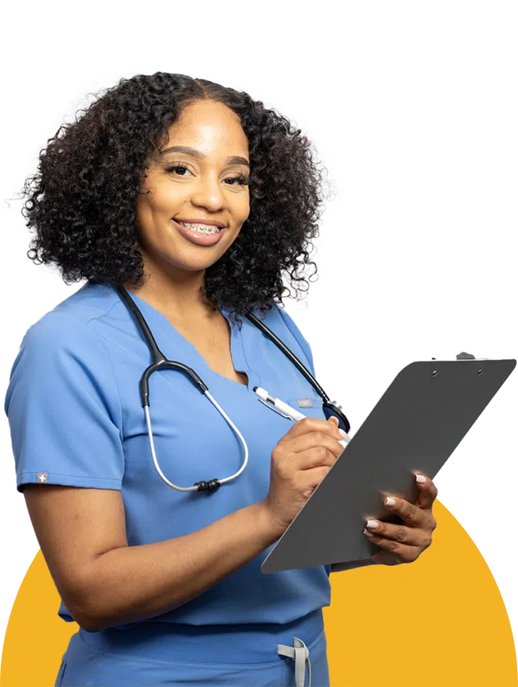 Female healthcare worker in scrubs smiling holding a clipboard and pen