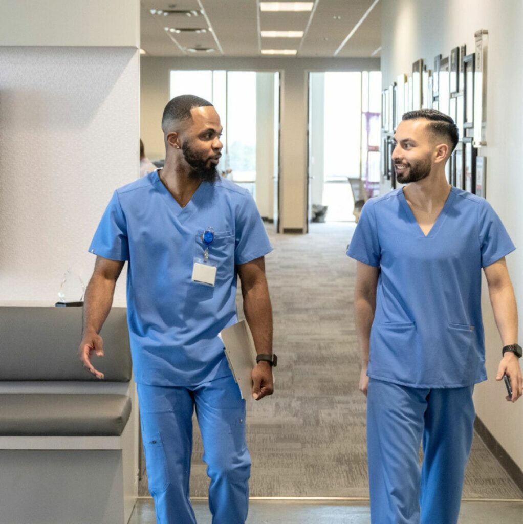 Photo of two male healthcare workers walking down a hallway and talking with each other