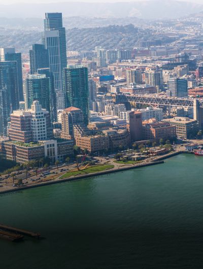 Overhead view of a bustling urban cityscape with a mix of modern skyscrapers and traditional buildings, adjacent to a large body of water, highlighting the contrast between the developed city and the natural waterfront